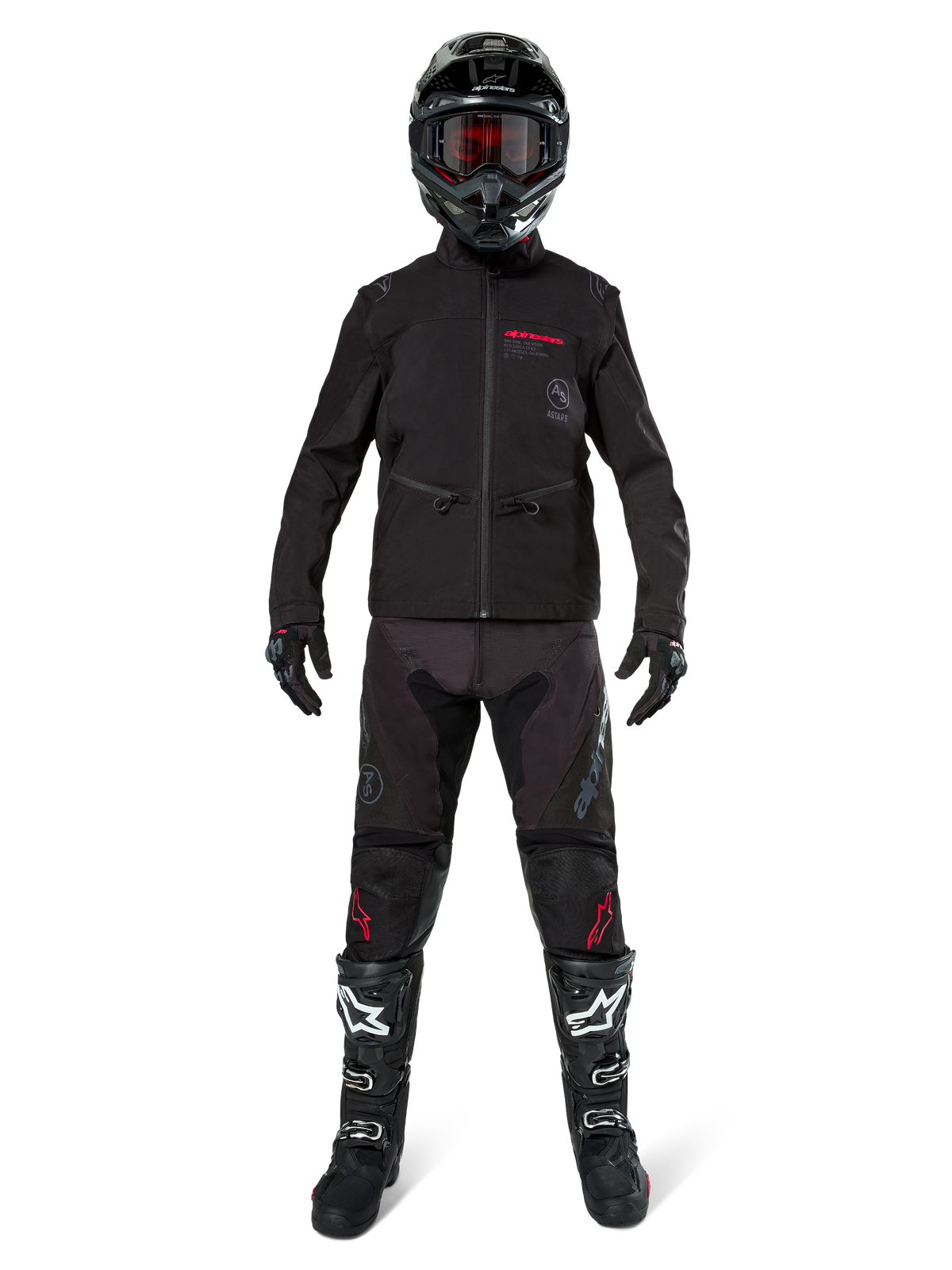 Pilota di motocross con Giacca Softshell Alpinestars Lite-Dura in nero e dettagli del logo rossi, abbinata a pantaloni off-road neri coordinati, casco nero e stivali bianchi e neri, abbigliamento professionale completo da enduro