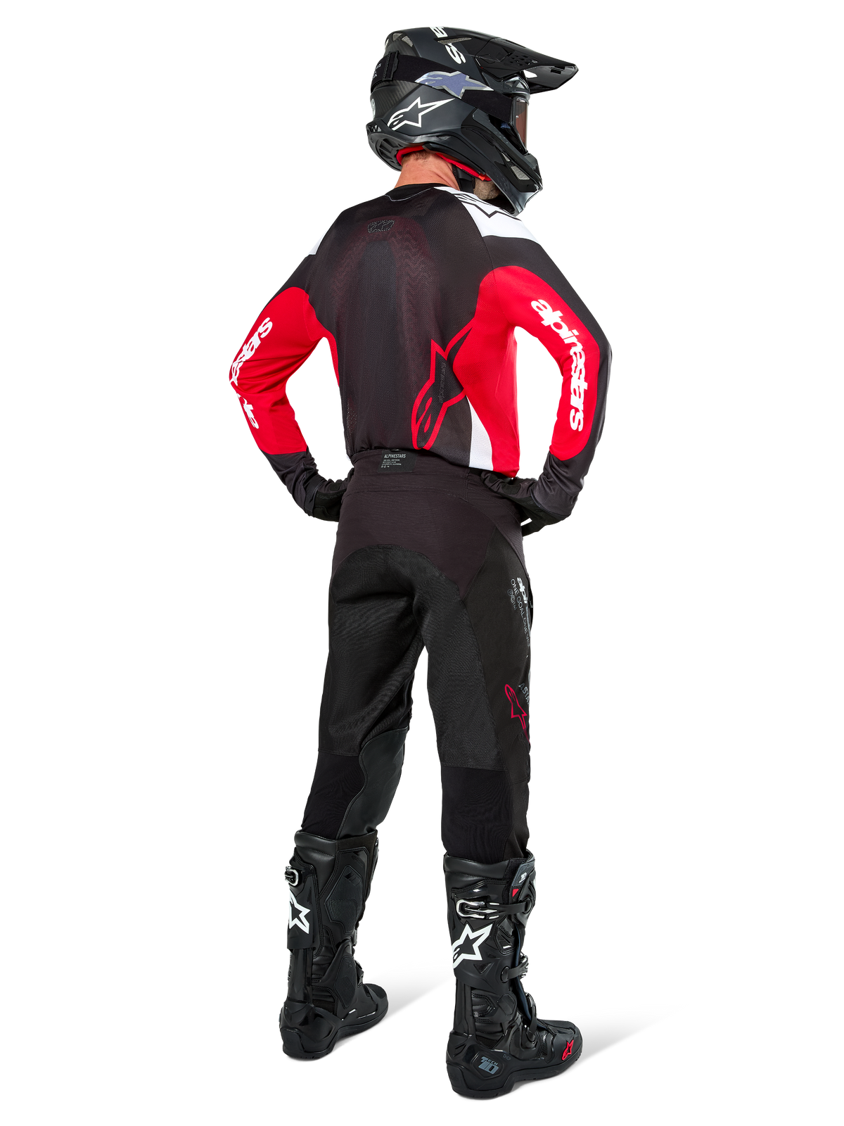 Pilota di motocross visto da dietro che indossa i pantaloni Alpinestars Pro-Dura in Black Magnet White, abbinati a una maglia rossa e nera e stivali neri, set di abbigliamento off-road coordinato per la guida enduro