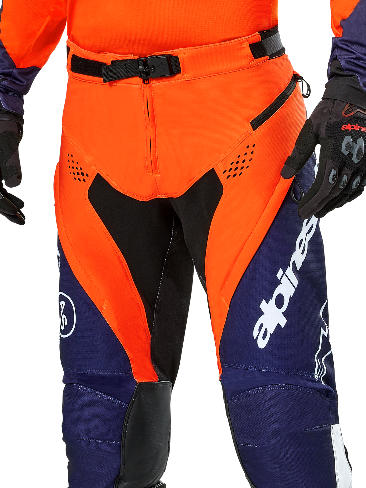 Alpinestars Pro-Dura Pants, pantaloni da moto enduro, blu navy, arancione acceso e bianco, vista del dettaglio della vita con fibbia magnetica SX2 e prese d'aria con zip sulle cosce, materiale ripstop resistente con branding evidente, indossati con abbigliamento coordinato