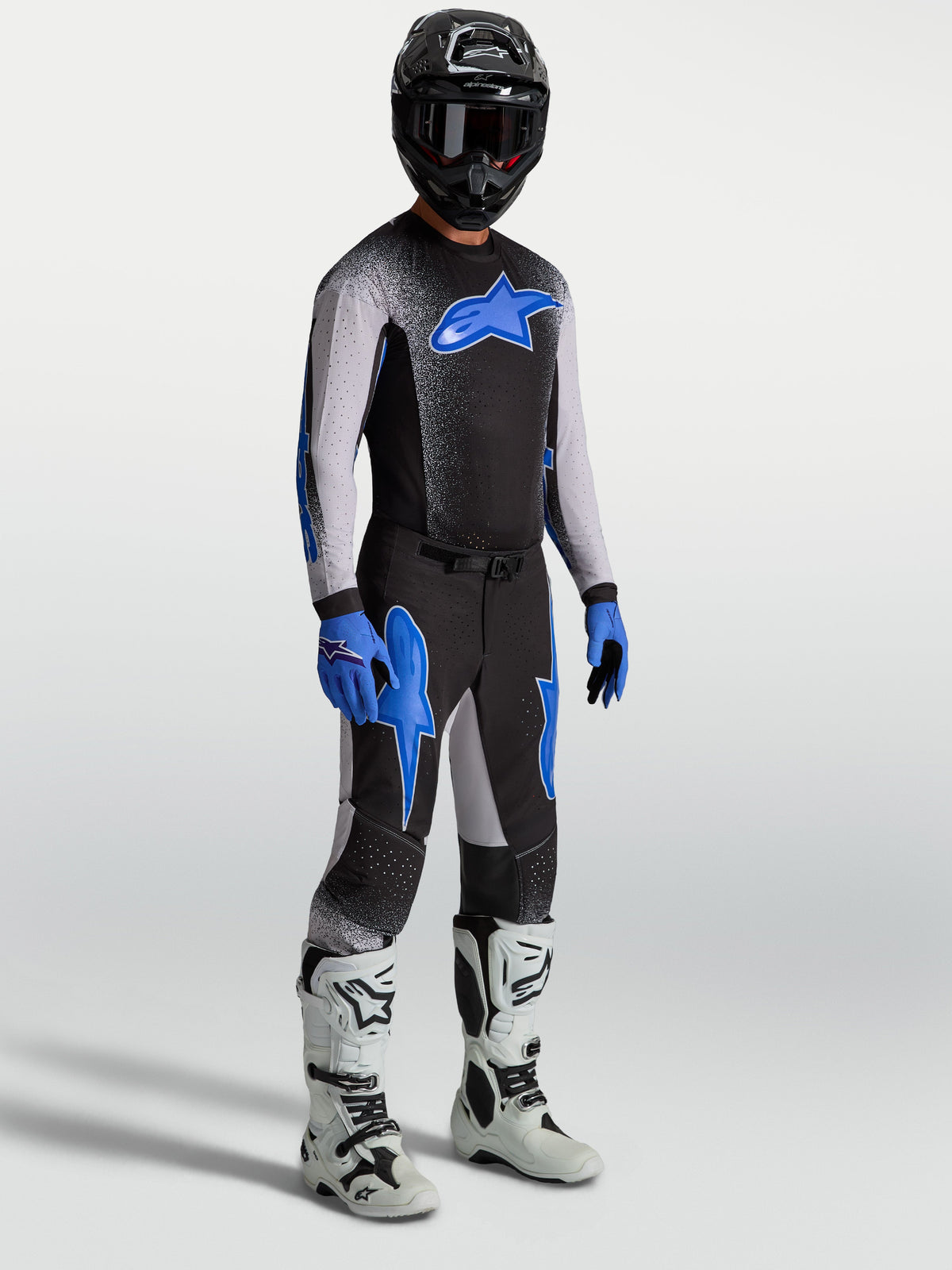 Pantaloni Alpinestars Supertech Hiten AFD, pantaloni da motocross neri e blu, indossati con maglia coordinata e stivali bianchi.