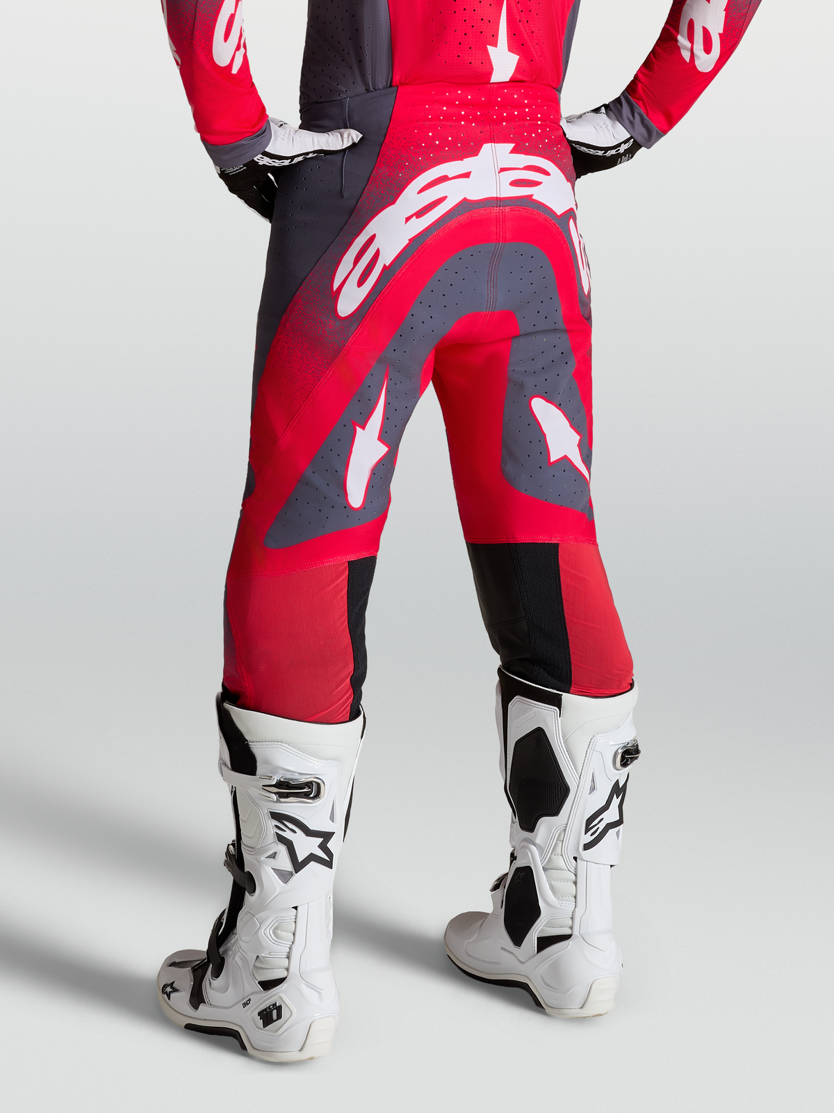 Alpinestars Pantaloni Supertech Hiten AFD, pantaloni da motocross rossi e grigi, vista posteriore su modello con stivali racing bianchi.