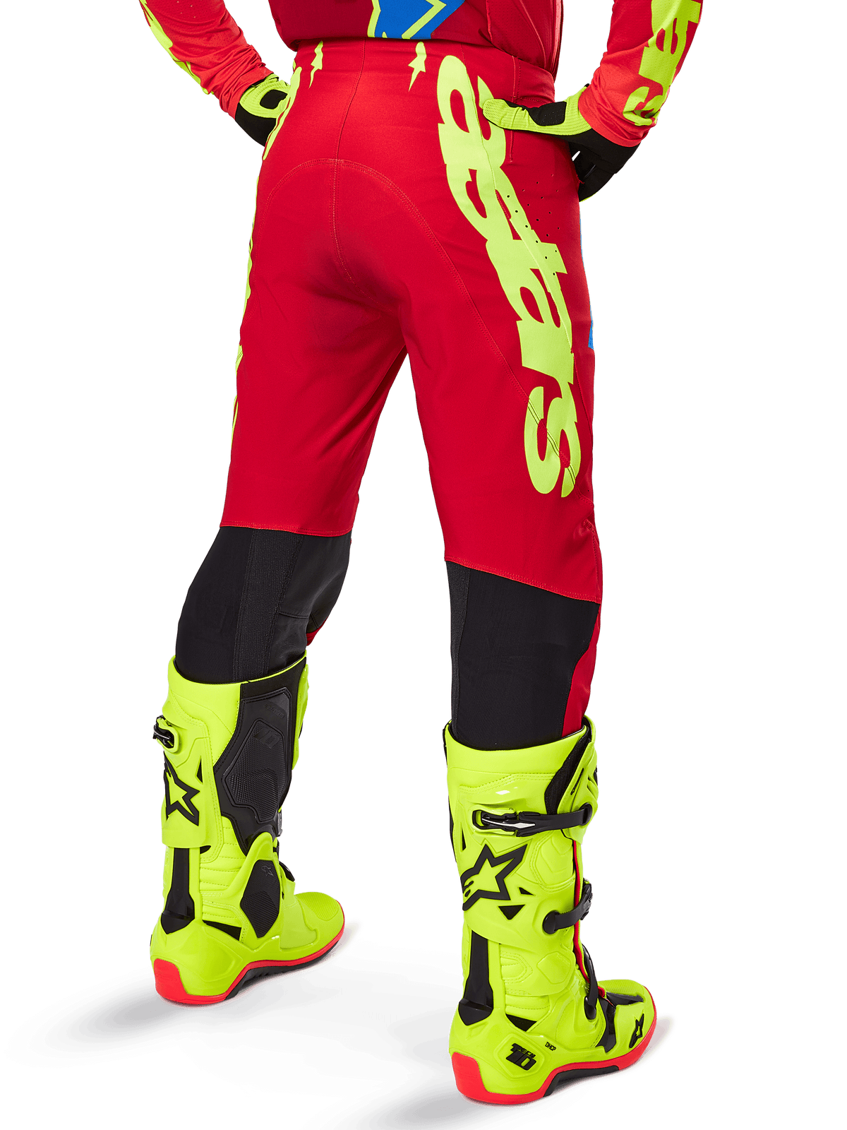 Alpinestars 2025 Supertech Maker Pants, pantaloni da motocross, rosso acceso e giallo fluo, vista posteriore che mostra il grande logo giallo sul lato e i pannelli neri sulla parte inferiore delle gambe, indossati con stivali e attrezzatura giallo fluo coordinati
