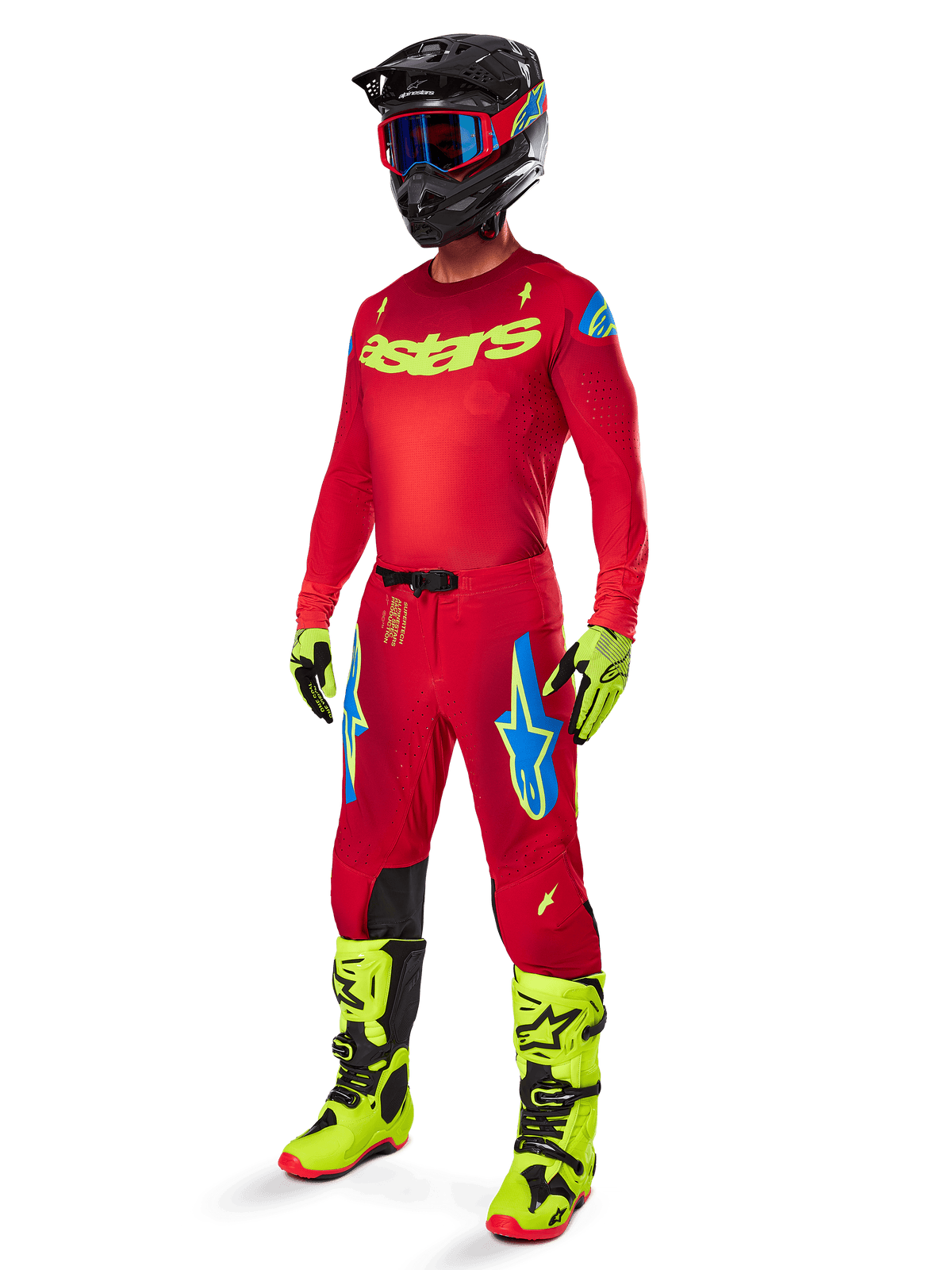 Pilota di motocross con abbigliamento completo Alpinestars, pantaloni Supertech Maker 2025 in rosso acceso e giallo fluo, maglia rossa coordinata con logo giallo neon, stivali giallo neon e neri, casco nero con occhiali blu, outfit professionale per gare fuoristrada
