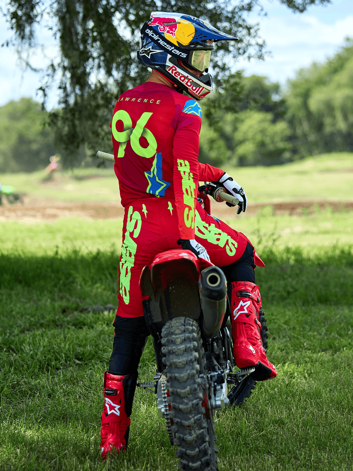 Pilota di motocross seduto su una moto da cross rossa, pantaloni Alpinestars 2025 Supertech Maker in rosso vivace e giallo fluo, maglia rossa coordinata con '96' e 'LAWRENCE' sul retro, stivali da gara rossi e casco marchiato Red Bull, set di abbigliamento professionale da gara fuoristrada