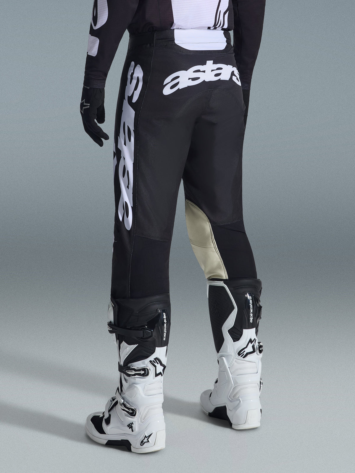 Alpinestars 2026 Racer Air Riway Pants, pantaloni da motocross, bianco e nero, vista posteriore con grande marchio Astars bianco sulla seduta e sulle gambe, pannelli interni del ginocchio in pelle tan, indossati con stivali Tech 7 bianchi e neri, abbigliamento premium per corse fuoristrada