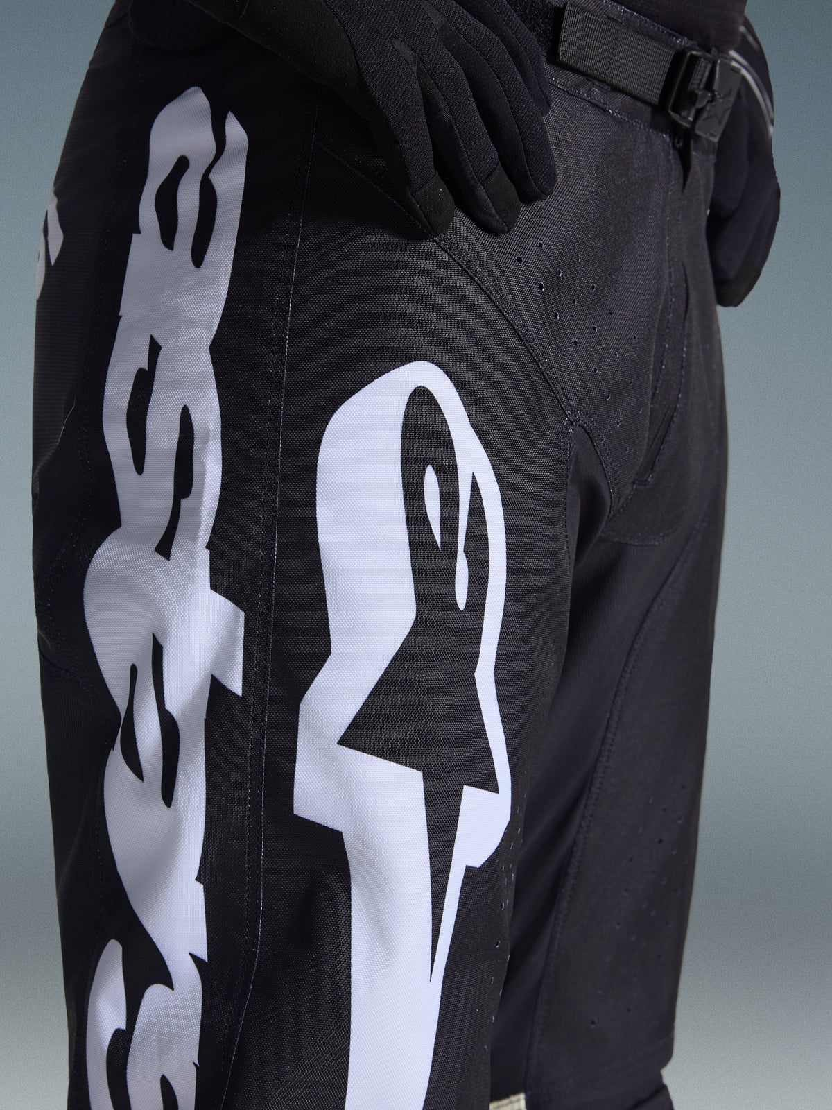 Pantaloni Alpinestars 2026 Racer Air Riway, pantaloni da motocross, nero e bianco, vista ravvicinata con grande logo Alpinestars bianco, perforazioni laser per la ventilazione e fibbia regolabile in vita, tessuto resistente per la guida fuoristrada