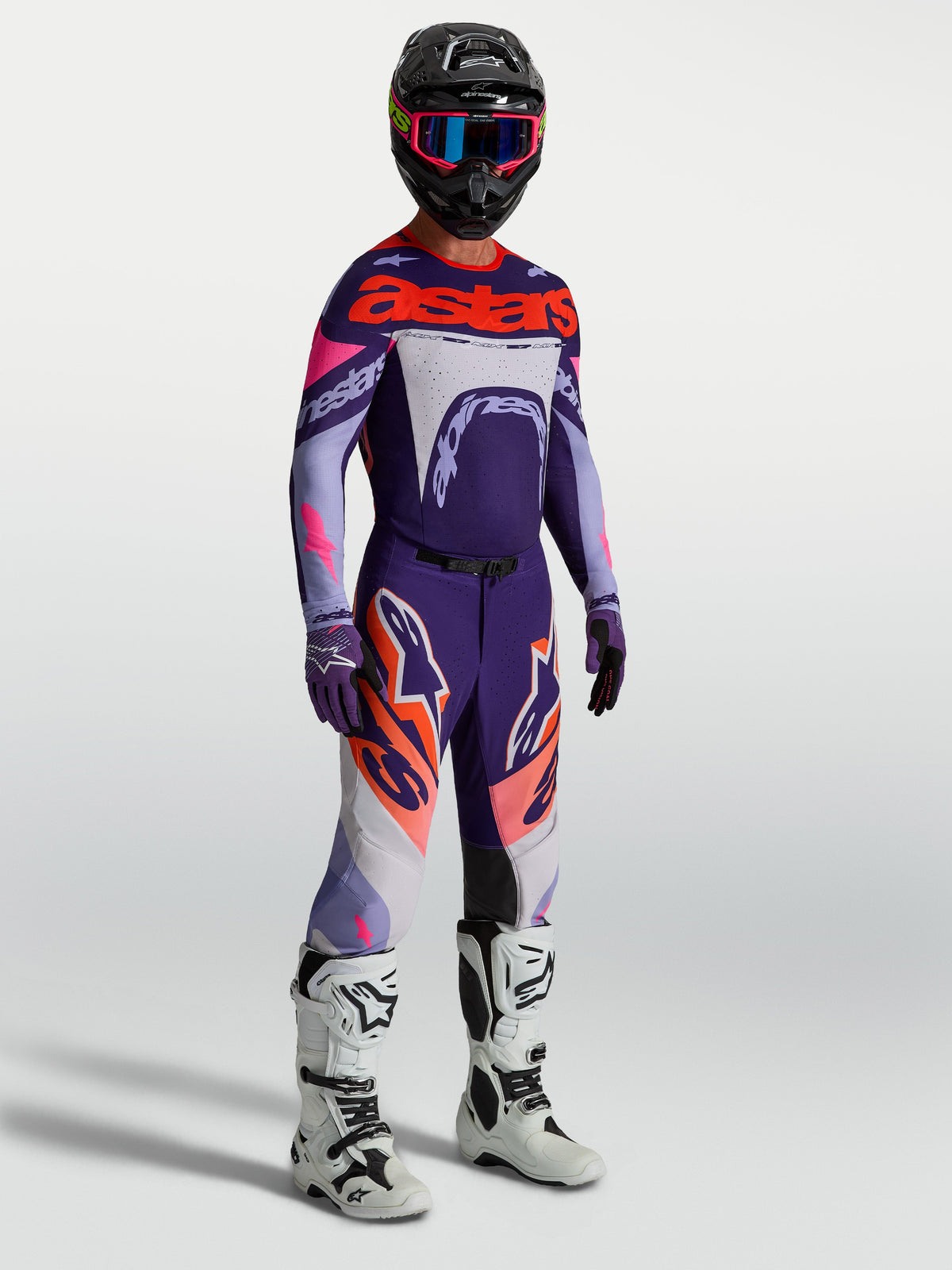 Alpinestars Pantaloni Supertech Dyna, pantaloni motocross uomo viola e rosa fluo, con maglia coordinata e stivali bianchi.