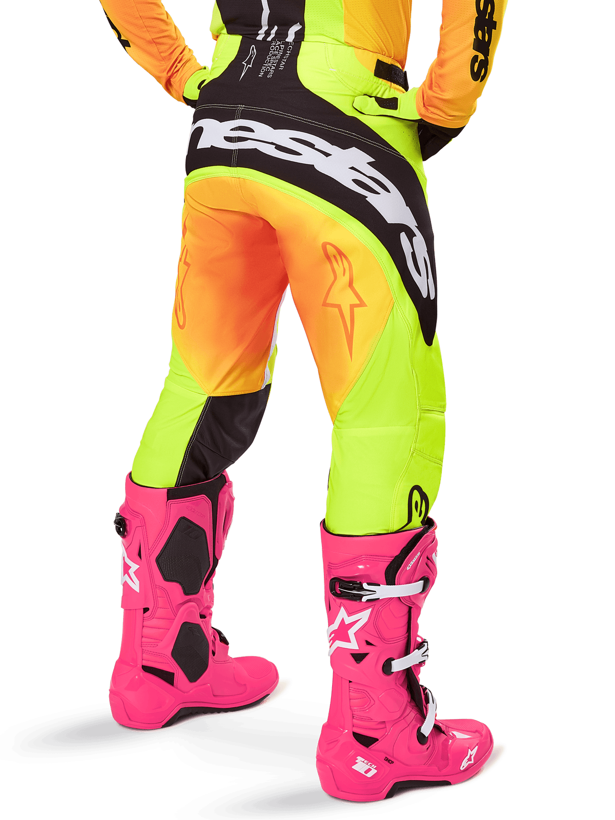 Vista posteriore di un pilota di motocross che indossa i pantaloni Alpinestars 2025 Techstar Melt, sfumatura gialla e arancione con logo nero e bianco sulla seduta, abbinati a stivali da motocross rosa acceso, abbigliamento tecnico da fuoristrada