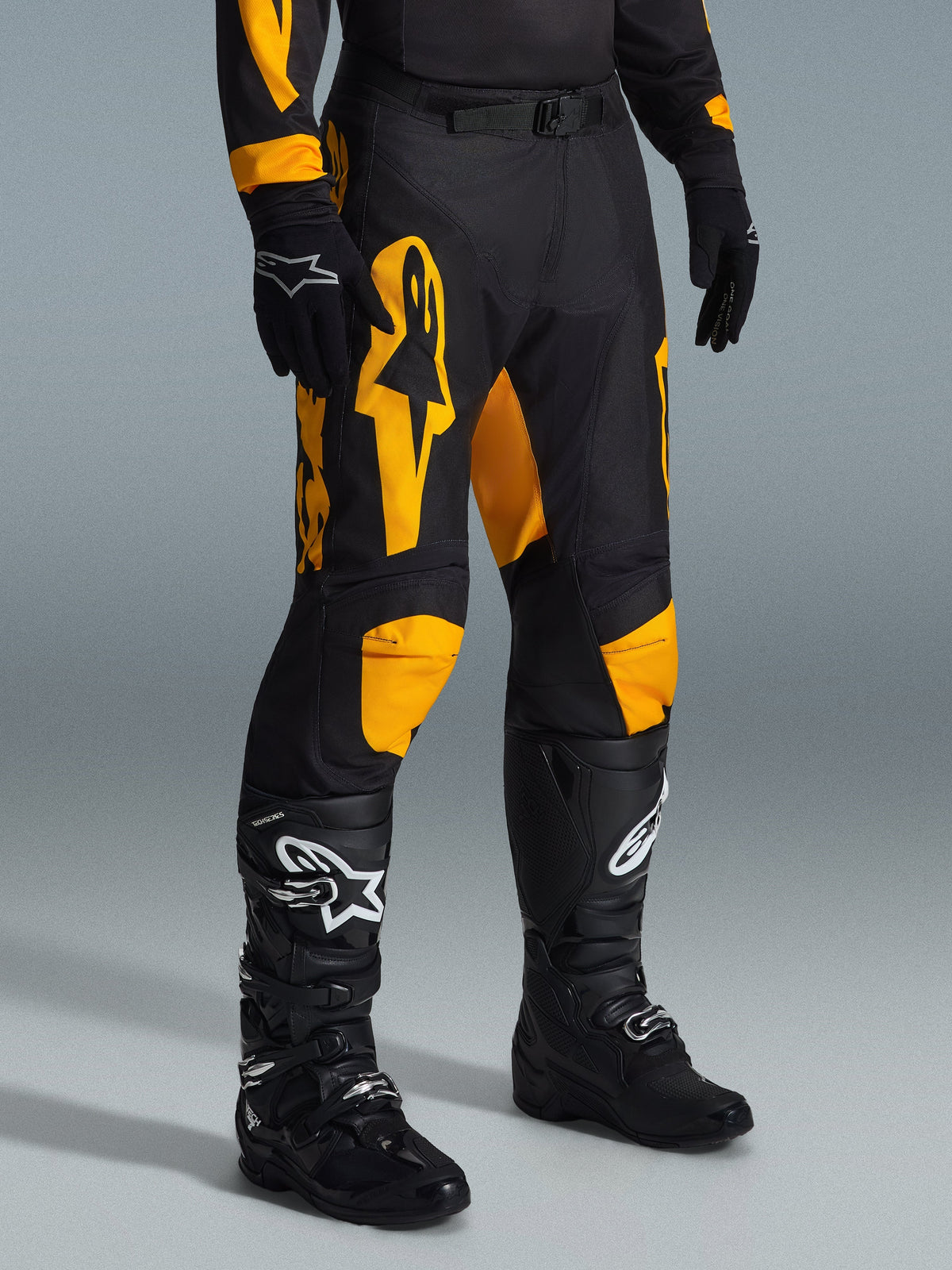 Pantaloni Alpinestars Racer Riway 2026, pantaloni da motocross, giallo e nero, indossati con guanti neri e stivali da motocross neri, con vistoso marchio Alpinestars giallo e inserti sulle ginocchia su base nera, progettati per corse off-road ad alte prestazioni