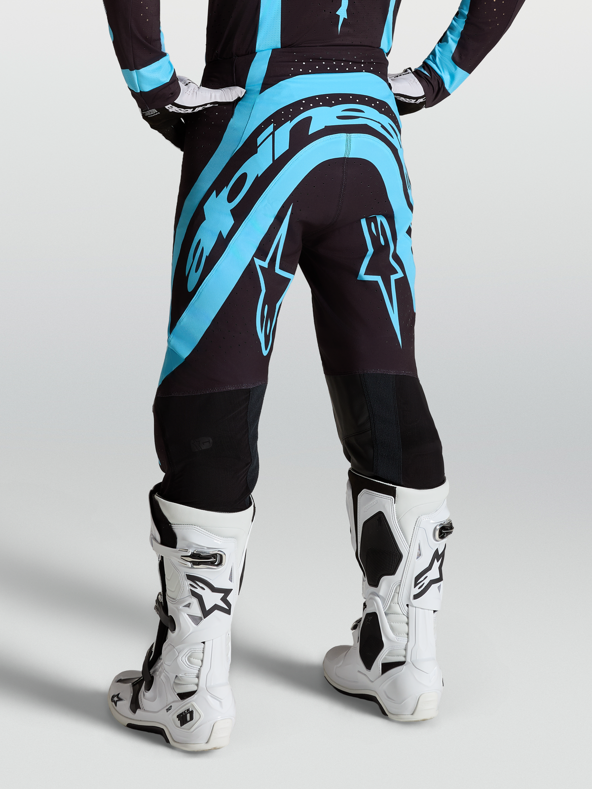 Alpinestars Pantaloni Supertech Vesta, abbigliamento motocross professionale, nero e turchese, vista posteriore su modello con stivali bianchi, vestibilità atletica da gara per prestazioni MX.