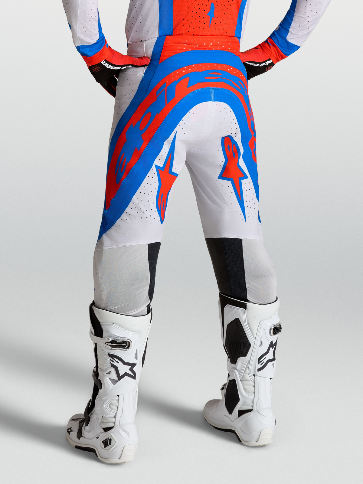 Alpinestars Pantaloni Supertech Vesta, pantaloni da motocross professionali bianchi, rossi e blu, visti dal retro, realizzati in tessuto rip-stop elasticizzato perforato con logo della stella.