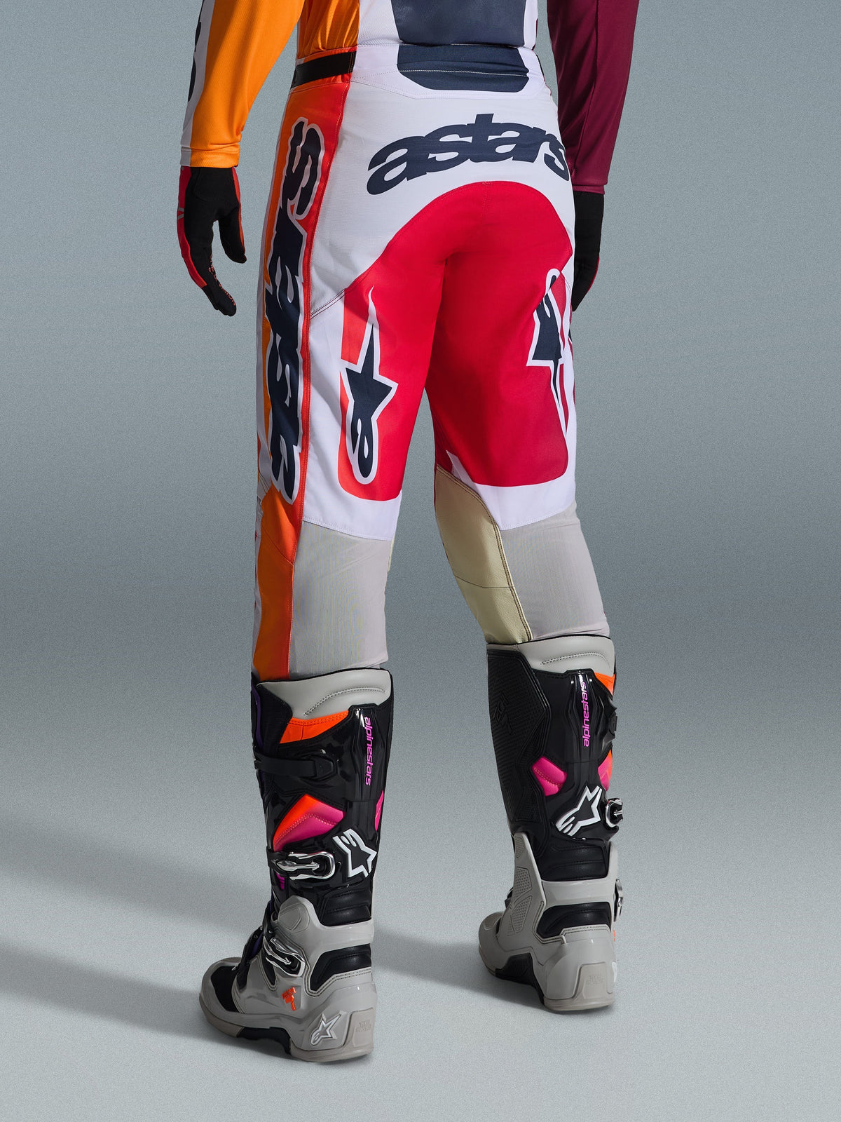Pantaloni Alpinestars Racer Portl 2026, pantaloni da motocross, rosso, grigio chiaro e grigio scuro, vista posteriore con loghi e branding audaci, abbinati a stivali e guanti da motocross coordinati, abbigliamento tecnico per gare fuoristrada.