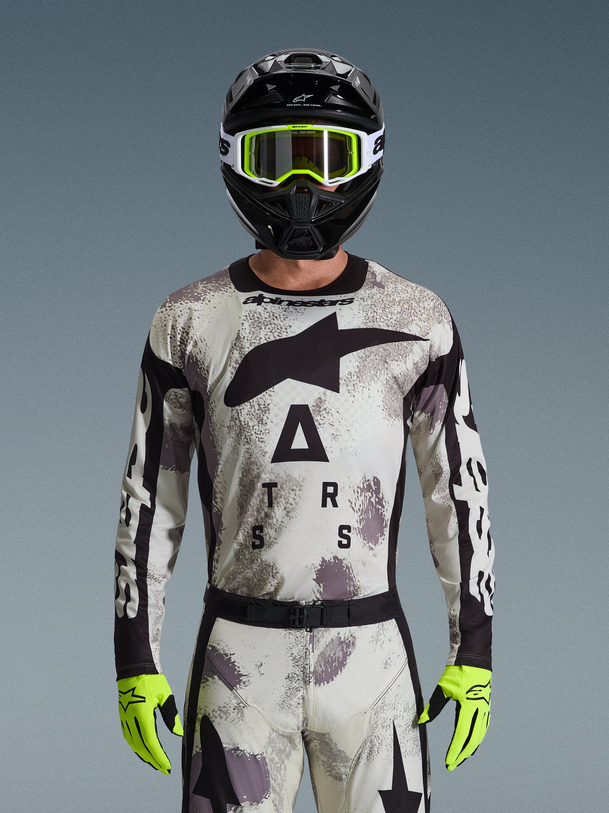 Alpinestars 2026 Racer Lahnd Jersey, completo da motocross, motivo Sand Camo grigio e bianco, grande logo a stella nero e scritta 'ASTARS', indossata con casco nero, occhiali giallo neon e guanti giallo neon, abbigliamento professionale da gara fuoristrada