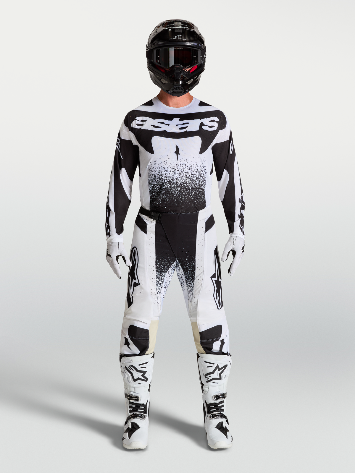 Alpinestars Pantaloni Techstar Swan e maglia, completo da motocross bianco e nero con stivali e casco coordinati su un modello, abbigliamento tecnico off-road.