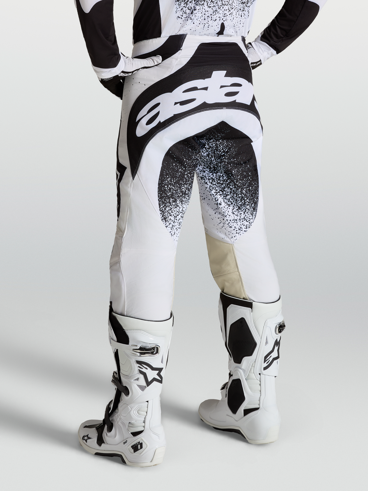Alpinestars Pantaloni Techstar Swan, pantaloni da motocross professionali da uomo, nero e bianco, design ergonomico con marchio Astar sul retro, indossati con stivali Tech 10 bianchi.
