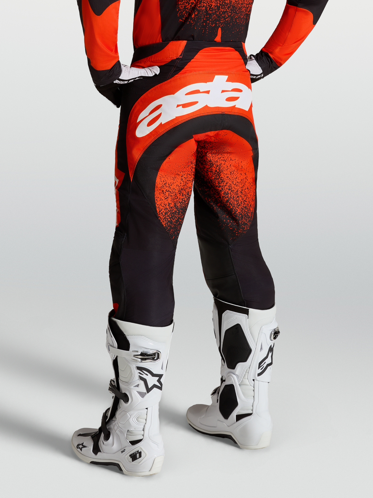 Pantaloni Techstar Swan Alpinestars, pantaloni motocross da uomo, rosso cardinale e nero, con branding Astar bianco sul retro e stivali Tech 10 bianchi.