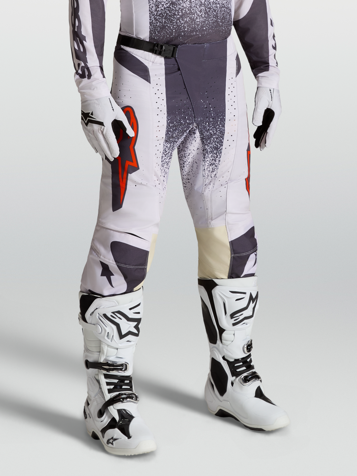 Alpinestars Pantaloni Techstar Swan, pantaloni da motocross da uomo, lilla chiaro e grigio scuro con dettagli rosso fluo, indossati con guanti e stivali bianchi, abbigliamento tecnico per off-road e competizioni