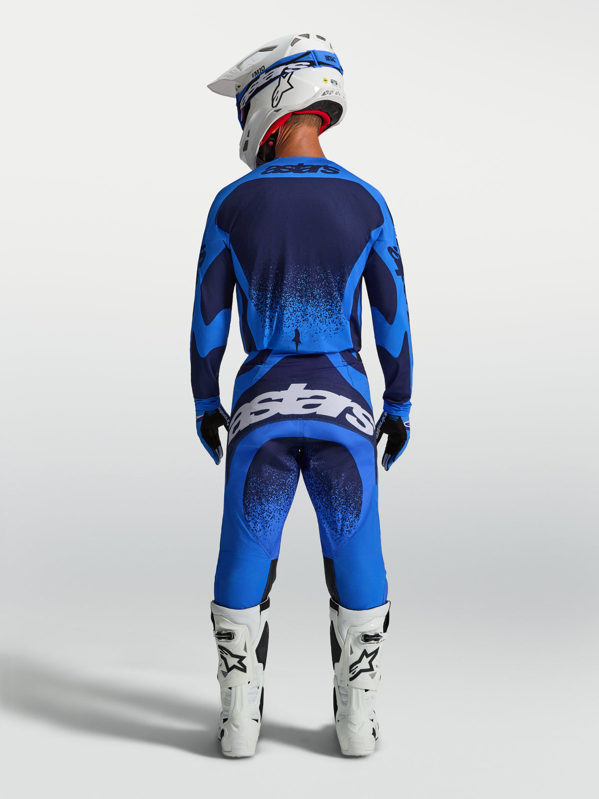 Alpinestars Pantaloni Techstar Swan, pantaloni da motocross da uomo, blu e blu scuro, visti dal retro con stivali bianchi.
