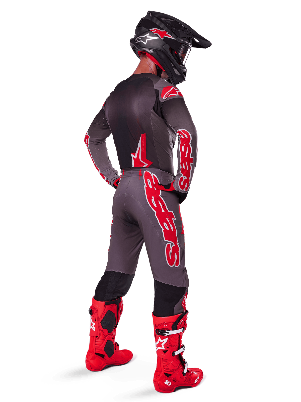 Pilota di motocross che indossa pantaloni Alpinestars Supertech Lipan 2025, Smoke Bright Red, pantaloni grigi con grandi loghi rossi e pannelli interni neri, abbinati a maglia grigia coordinata, casco nero e stivali rosso brillante, completo da gara fuoristrada visto da dietro.