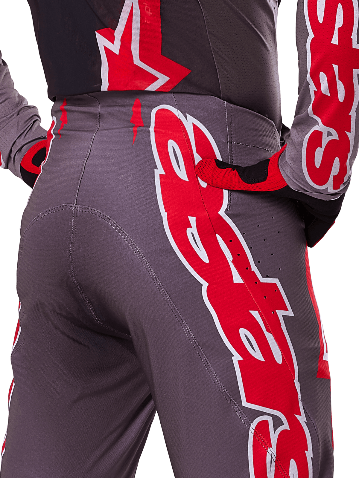 Alpinestars 2025 Supertech Lipan Pants, pantaloni da motocross, Smoke Bright Red, vista ravvicinata posteriore che mostra il tessuto grigio scuro con grafiche rosse audaci, indossati con maglia e guanti rossi e neri coordinati, con perforazioni per la ventilazione e cuciture ergonomiche per prestazioni off-road