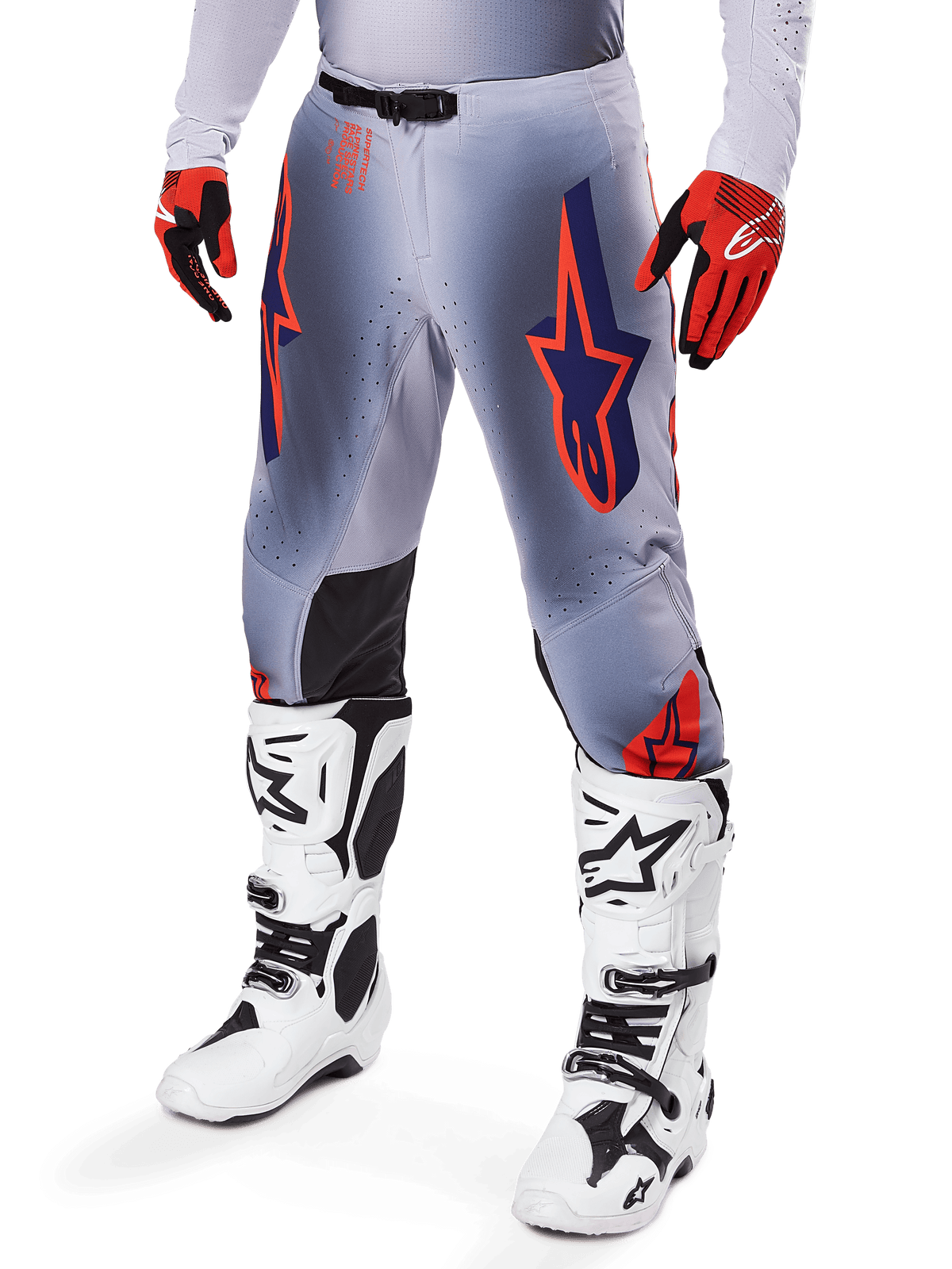 Pantaloni Alpinestars Supertech Lipan 2025, pantaloni da motocross, grigio e arancione fluo, con design a stelle blu navy e pannelli interni neri sulle ginocchia, indossati con guanti rosso-arancio e stivali bianchi, abbigliamento professionale da gara fuoristrada