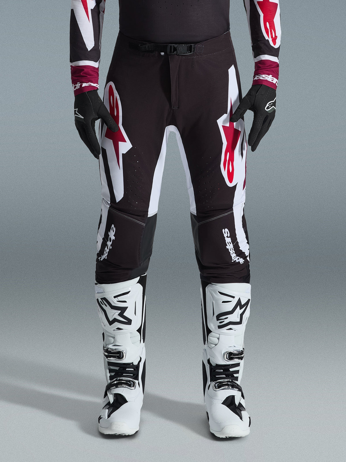 Alpinestars 2026 Supertech AFD Vista Pants, pantaloni da motocross, nero rosso e bianco, con grandi loghi grafici sulle cosce e sulle ginocchia, indossati con stivali da gara bianchi e guanti neri, design atletico race-ready per competizioni off-road d'élite