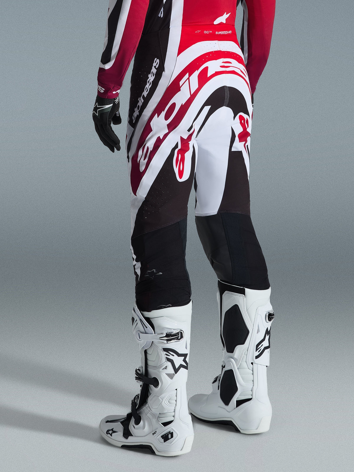 Alpinestars 2026 Supertech AFD Vista Pants, pantaloni da motocross, nero, rosso e bianco, vista posteriore con grande branding Alpinestars sulla seduta, abbinati a stivali Tech 10 bianchi e guanti neri, design atletico per prestazioni off-road d'élite