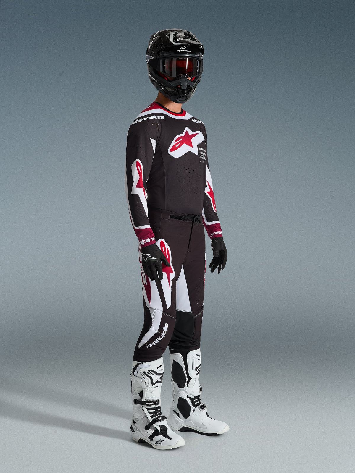 Alpinestars 2026 Supertech AFD Vista Pants, pantaloni da motocross, nero, rosso e bianco, indossati con maglia da gara coordinata, casco nero con occhiali rossi, guanti neri e stivali bianchi, abbigliamento sportivo ad alte prestazioni per corse fuoristrada