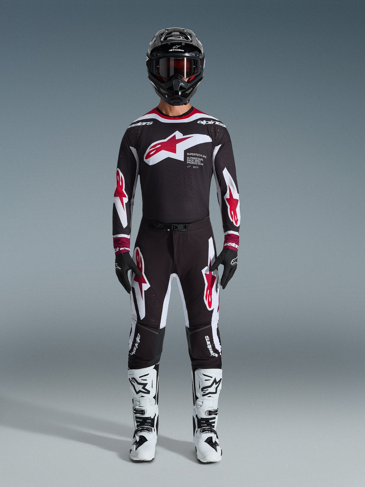 Pantaloni Alpinestars 2026 Supertech AFD Vista, pantaloni da motocross, nero, rosso e bianco, indossati come completo da gara con maglia coordinata, casco nero e stivali bianchi, con branding Astars rosso e bianco su petto e gambe, progettati per prestazioni off-road d'élite