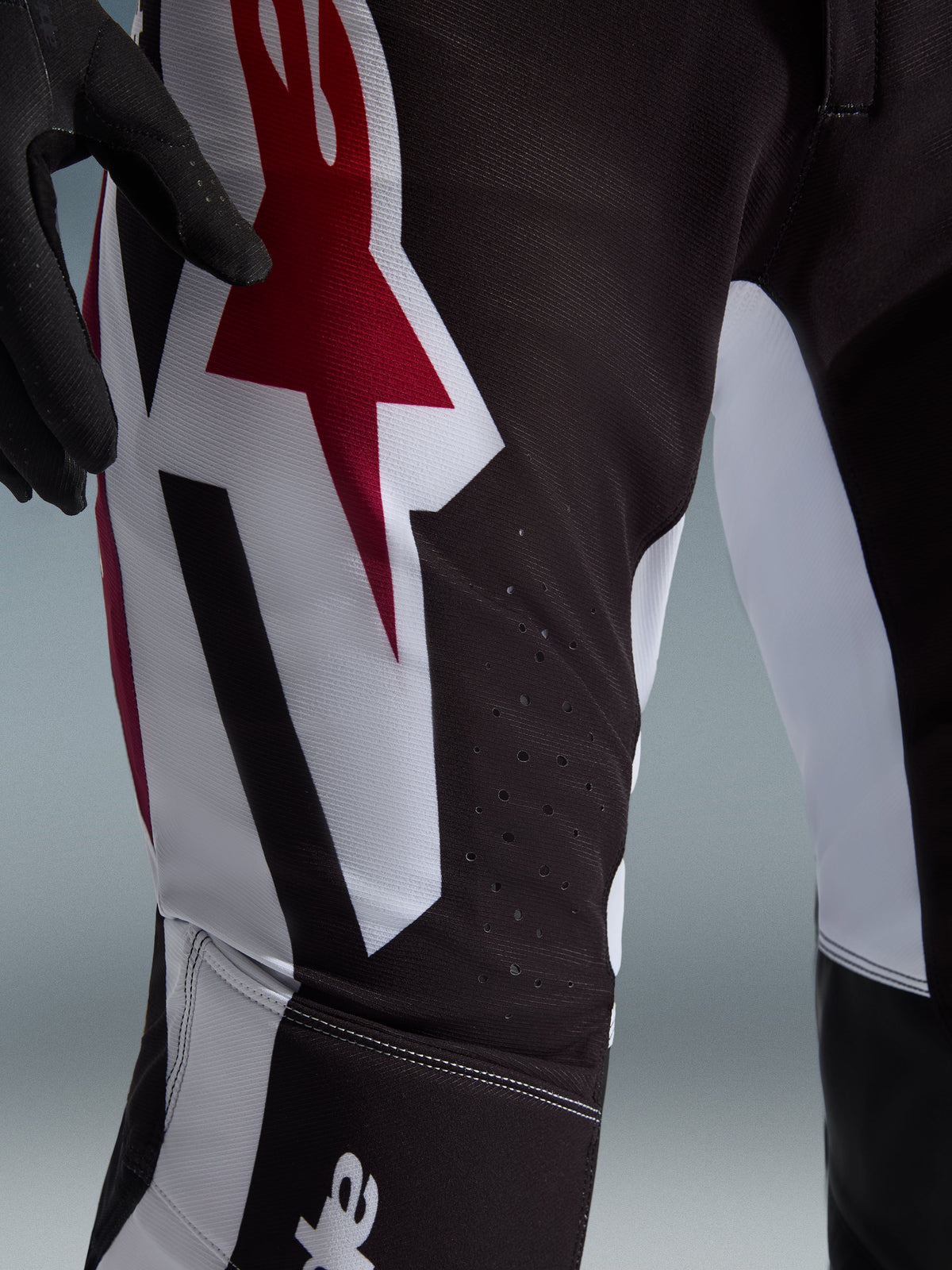 Alpinestars 2026 Supertech AFD Vista Pants, pantaloni da motocross, nero, rosso e bianco, primo piano della zona della coscia con grande logo a stella rosso e bianco, perforazioni tagliate al laser per la circolazione dell'aria e resistente tessuto ripstop elasticizzato.
