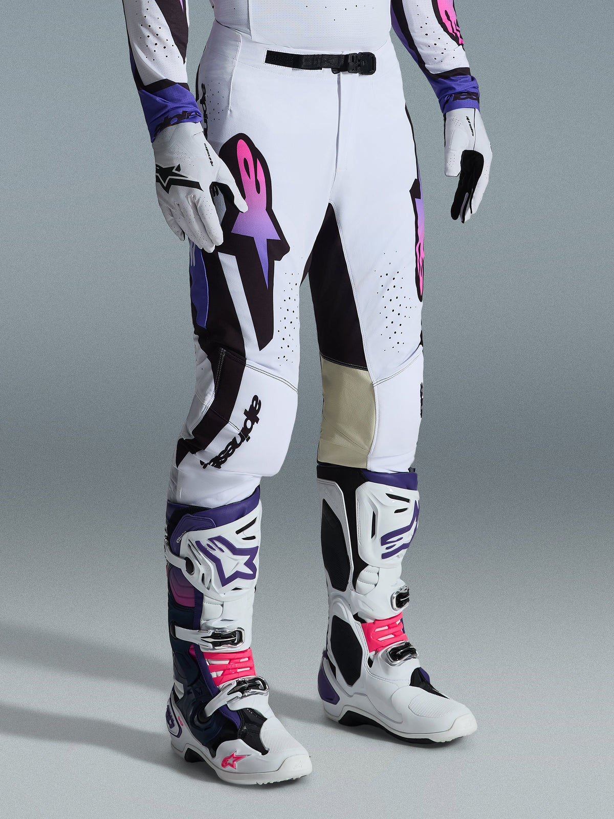 Alpinestars 2026 Supertech AFD Vista Pants, pantaloni da motocross, bianco, viola e nero, con logo Astar sfumato rosa e viola, indossati con stivali e guanti da motocross bianchi e viola coordinati, vestibilità atletica race con pannelli interni al ginocchio in pelle beige e dettagli traforati.