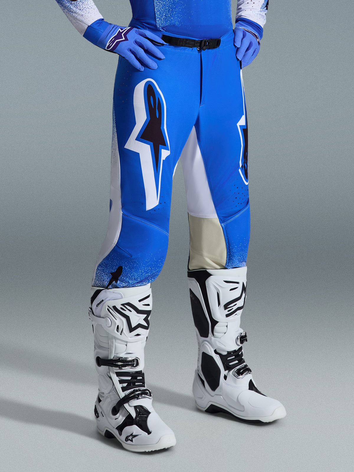 Alpinestars Pantaloni Supertech Scenz 2026, pantaloni da motocross, blu UCLA e bianco, indossati con stivali bianchi e neri e guanti blu, caratterizzati da grandi loghi grafici sulle cosce e pannelli bianchi, vestibilità atletica progettata per gare di motocross