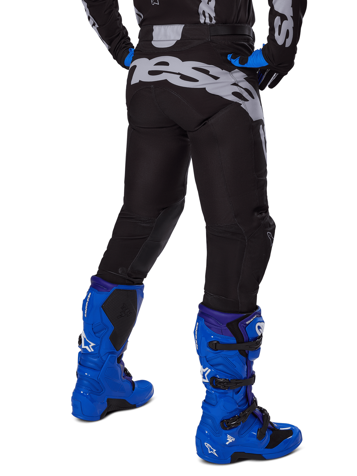 Alpinestars Pantaloni Racer Graphite 2025, pantaloni da motocross, nero e grigio, vista posteriore con grande logo grigio sulla seduta, indossati con stivali da motocross blu acceso e maglia nera e blu, abbigliamento da gara fuoristrada resistente
