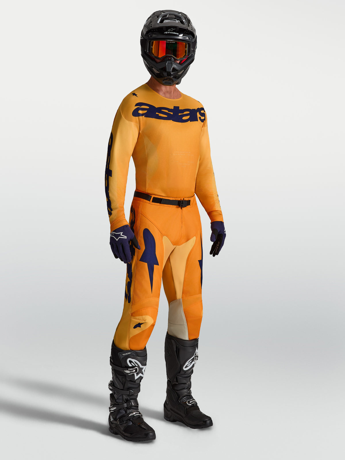 Alpinestars Pantaloni Racer Amber e maglia, abbigliamento da motocross da uomo, arancione e blu, con stivali e casco neri.