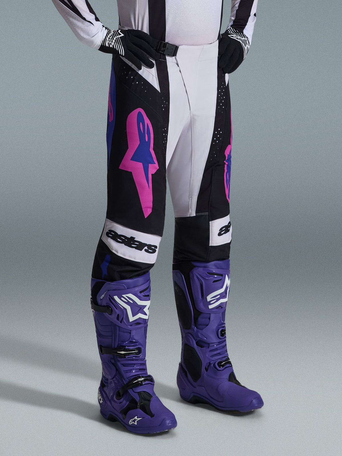 Alpinestars Techstar Knif Pants 2026, nero, grigio chiaro e viola, indossati con stivali da motocross viola coordinati, con vivaci accenti rosa e logo 'astars', abbigliamento professionale da gara per motocross