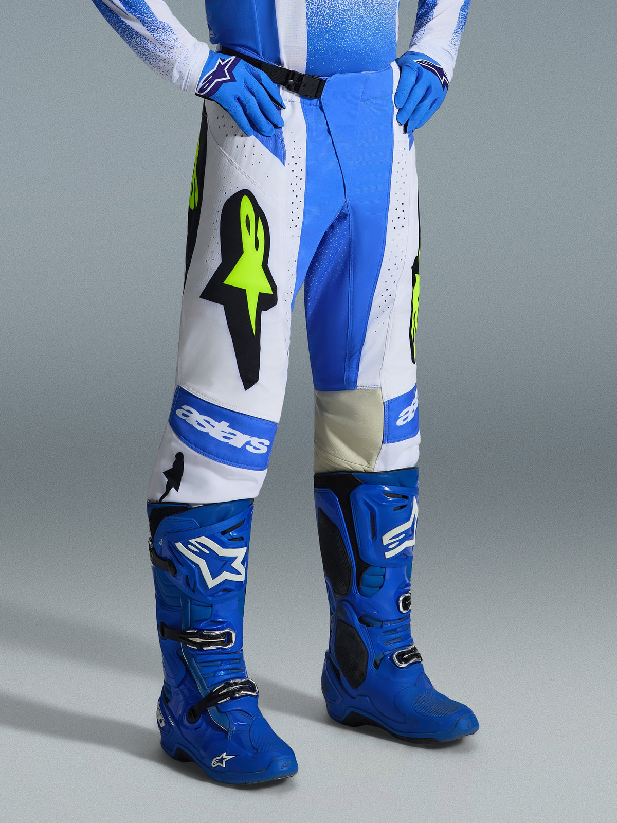Alpinestars 2026 Techstar Knif Pants, pantaloni da motocross, blu UCLA, bianco e nero con giallo fluo, indossati con stivali e guanti blu coordinati, con branding Alpinestars e loghi Astar, equipaggiamento ad alte prestazioni per gare off-road