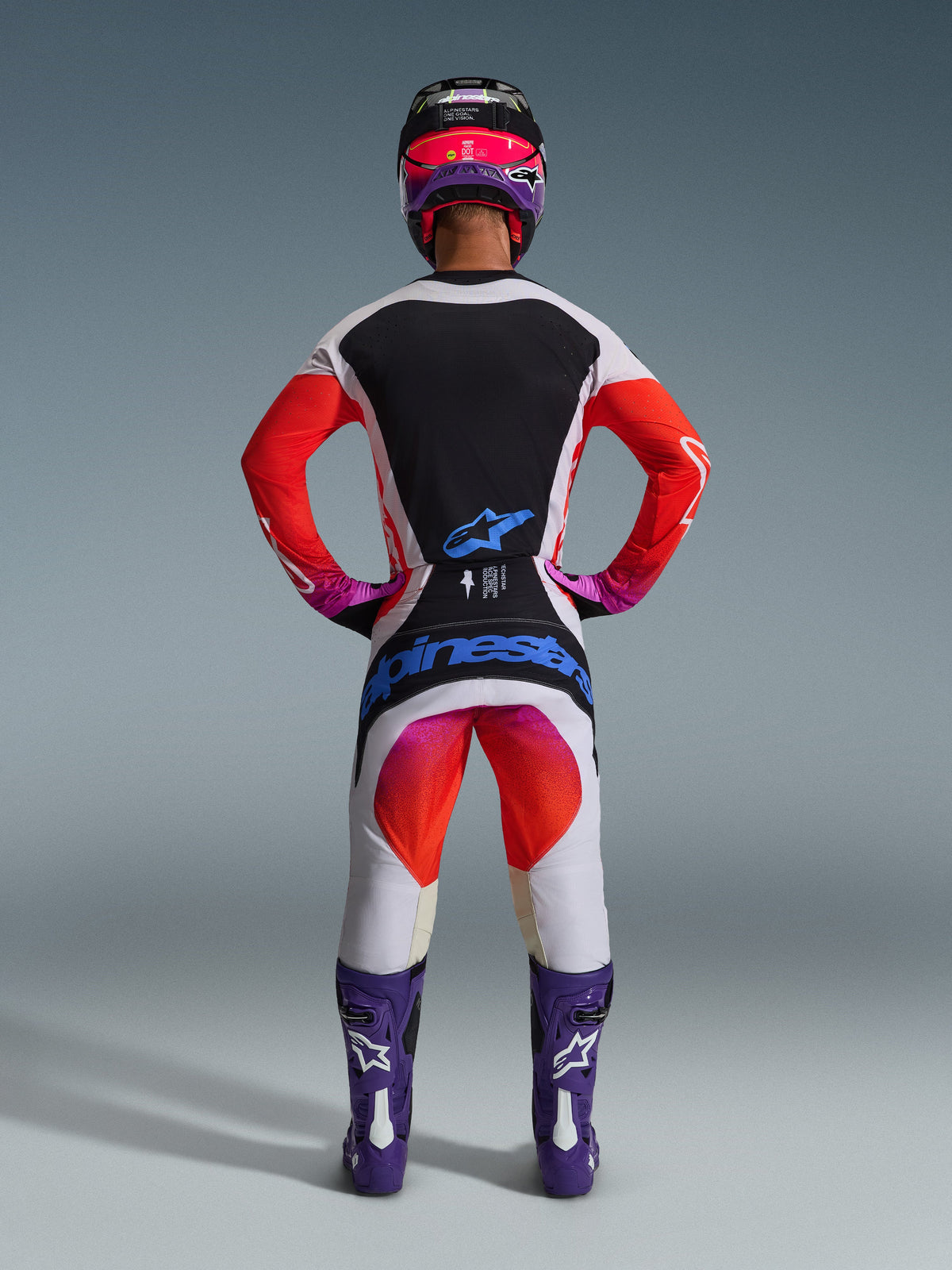 Set completo Alpinestars 2026 Techstar Knif, abbigliamento completo da motocross visto da dietro, maglia bianca e nera con maniche a sfumatura rossa, pantaloni bianchi con accenti rossi e rosa, coordinato con stivali viola e casco rosa, branding blu audace, kit professionale per corse fuoristrada