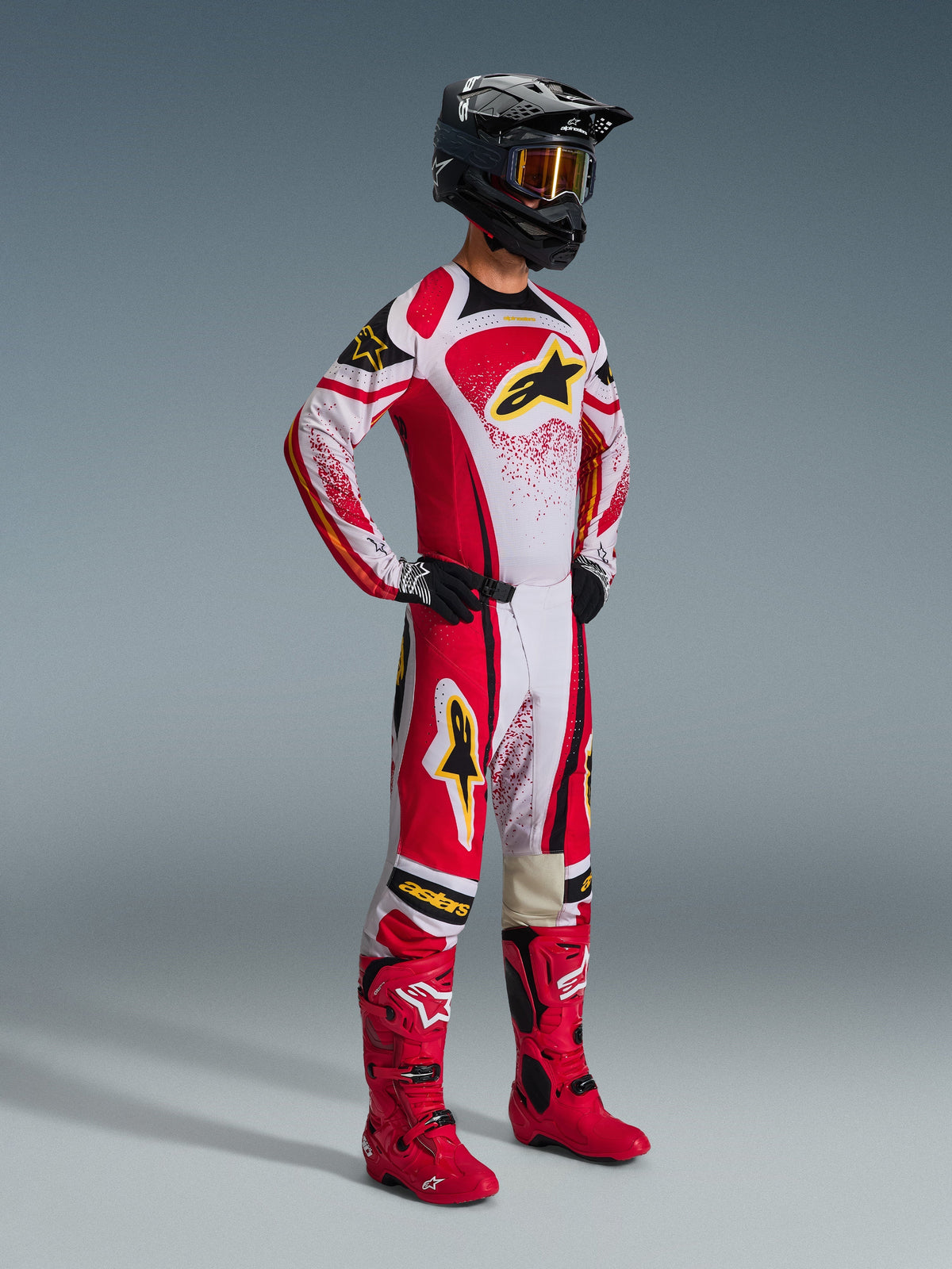 Pilota di motocross con abbigliamento completo da gara, maglia Techstar Nomur 2026 in rosso, bianco e nero, pantaloni da motocross coordinati con accenti gialli, casco nero con occhiali, stivali rossi e guanti neri, completo coordinato per corse fuoristrada