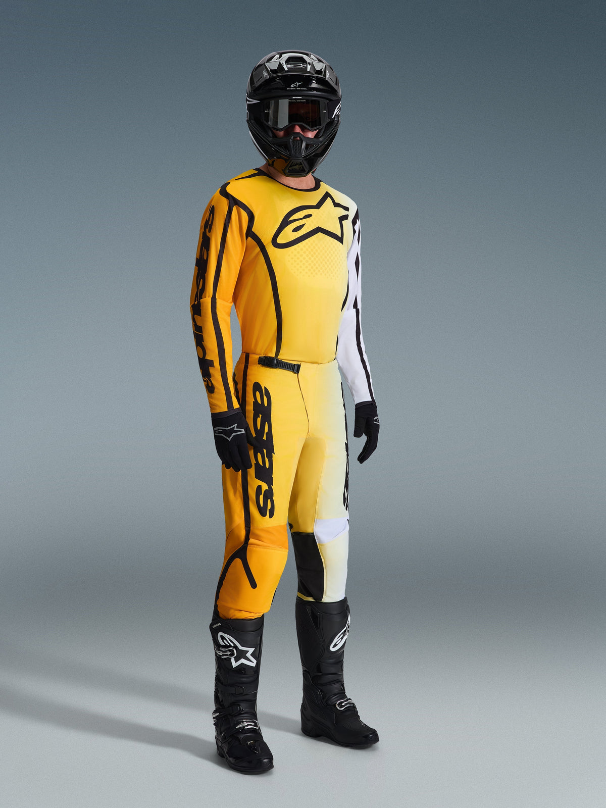 Pantaloni Alpinestars Fluid Apex 2026, pantaloni da motocross, giallo e nero, indossati con maglia coordinata gialla e bianca, casco nero, occhiali, guanti e stivali neri, con loghi neri e design sfumato moderno per il fuoristrada