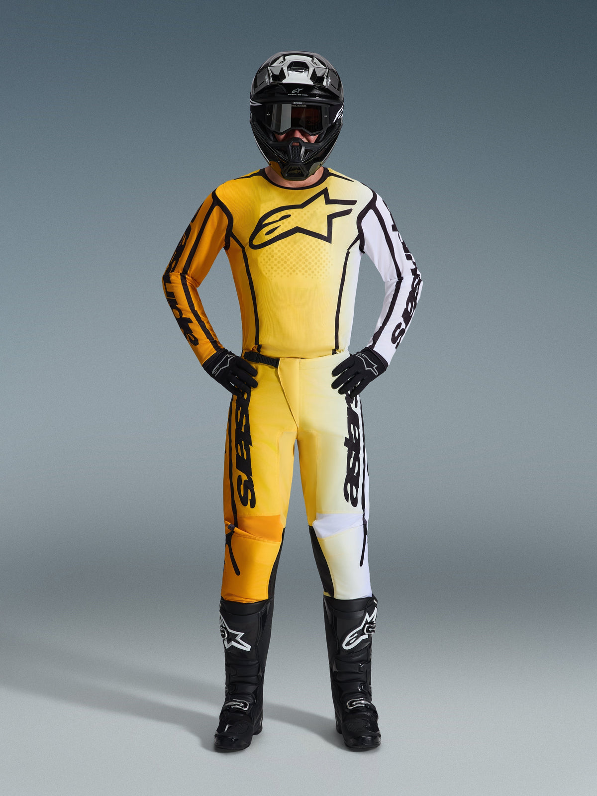 Alpinestars 2026 Fluid Apex Pants, pantaloni da motocross in giallo, nero e bianco, indossati come kit da gara completo con maglia sfumata coordinata, casco nero e stivali, abbigliamento professionale per fuoristrada