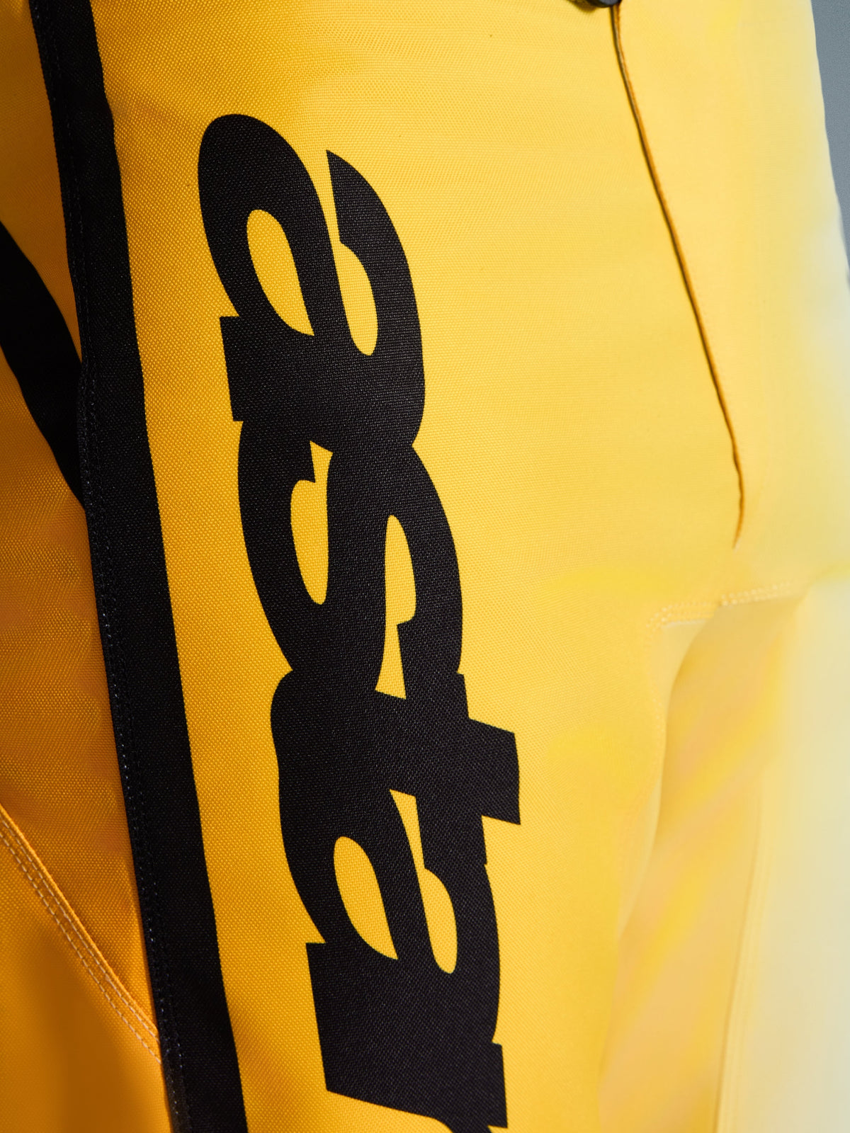 Primo piano dei pantaloni Alpinestars 2026 Fluid Apex, pantaloni da motocross, giallo e nero, con un grande logo nero verticale, materiale resistente e testurizzato e dettagli ergonomici per prestazioni off-road