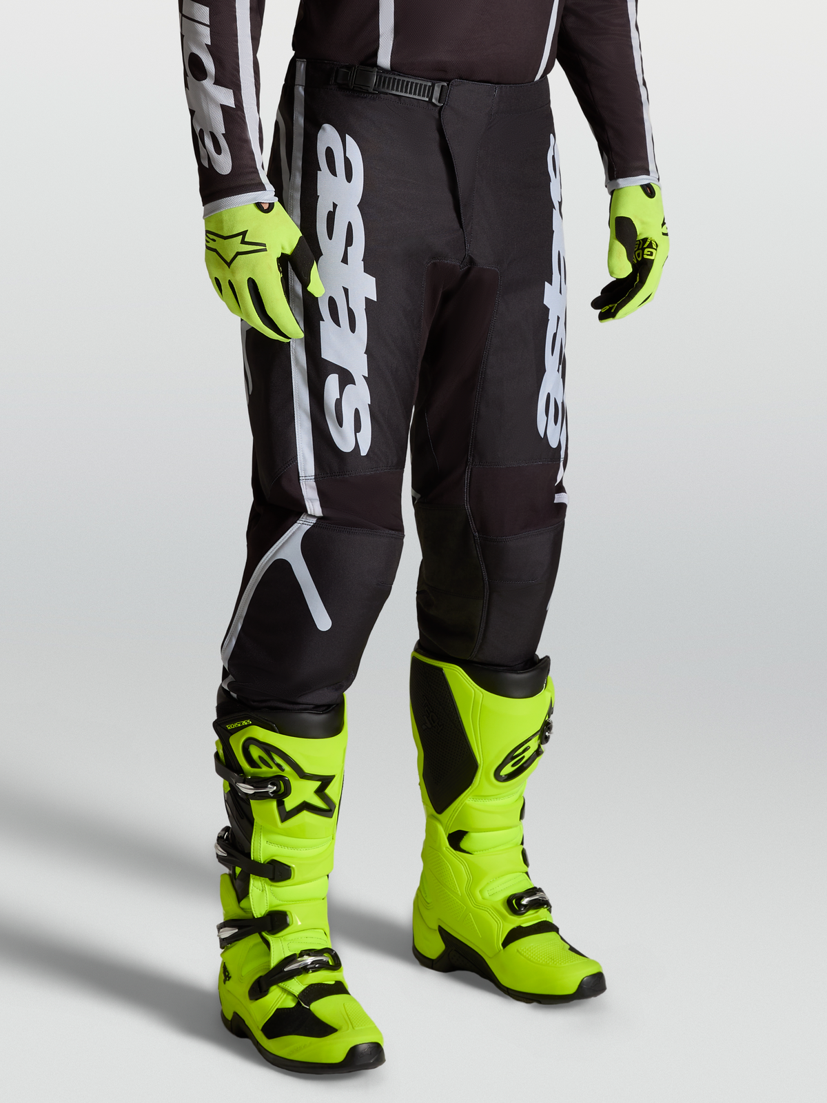 Alpinestars Pantaloni Fluid Apex V2, pantaloni motocross da uomo, nero e argento, indossati con stivali giallo fluo.
