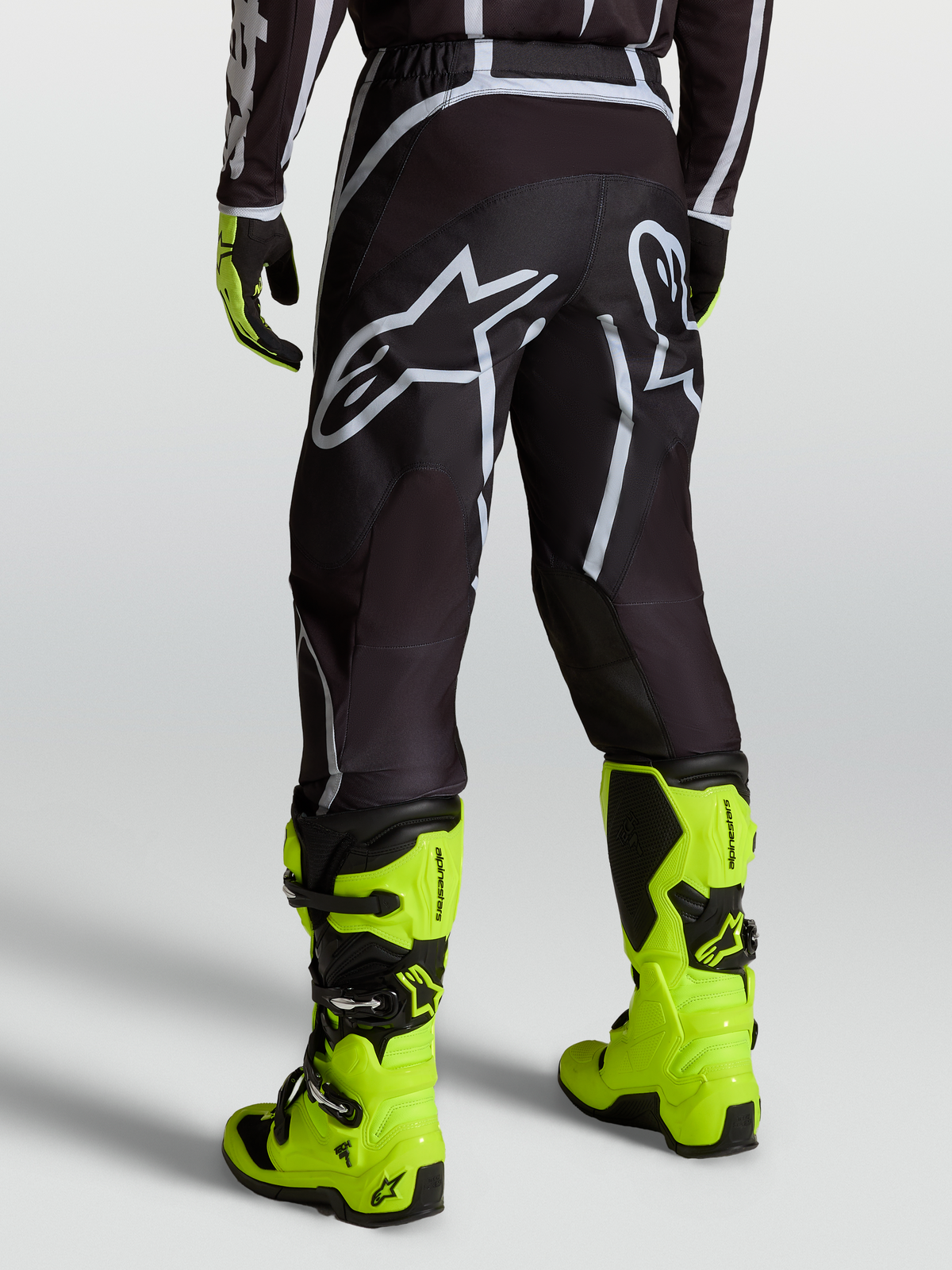 Alpinestars Pantaloni Fluid Apex V2, pantaloni da motocross da uomo, nero e argento con logo bianco, indossati con stivali giallo fluorescente