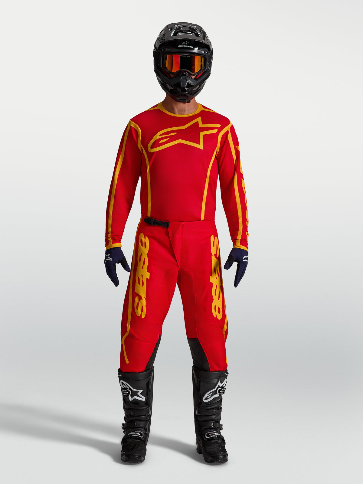 Alpinestars Pantaloni Fluid Apex V2, completo da motocross uomo rosso e oro con maglia abbinata, casco e stivali neri.