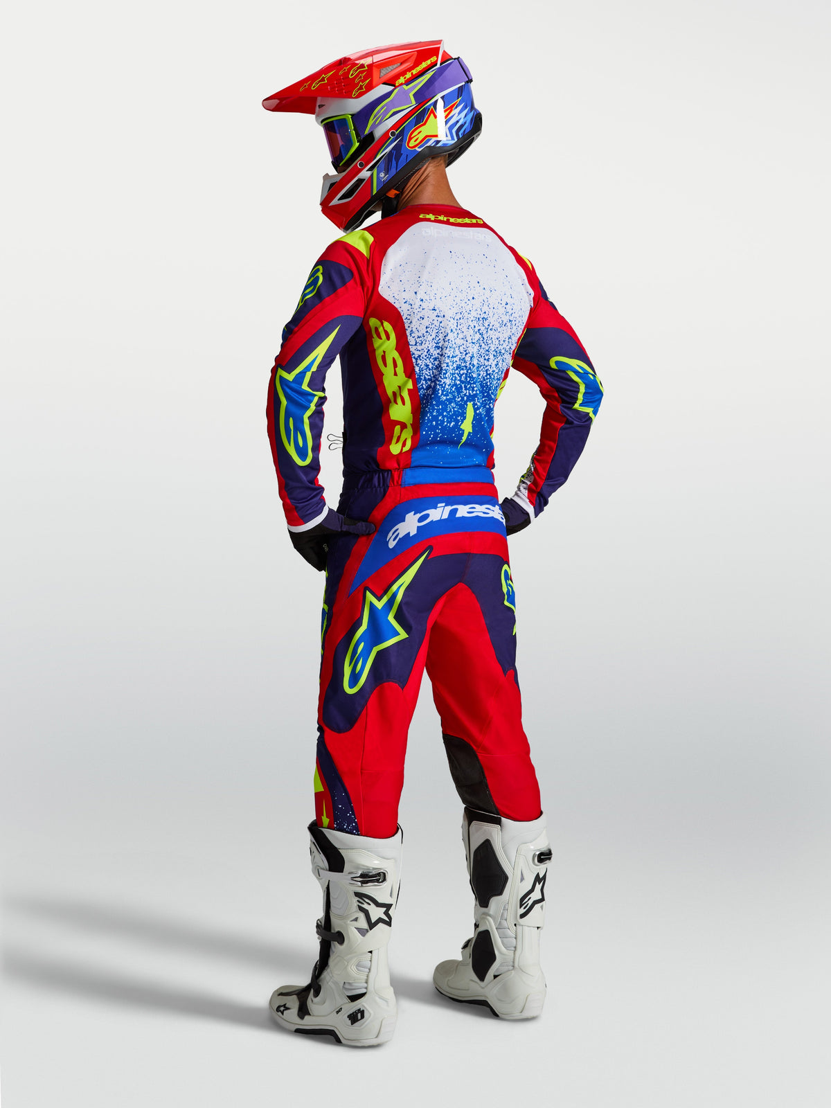 Alpinestars pantaloni e Gear Set Fluid Drag 2027, completo motocross uomo blu e rosso, stivali bianchi, vista posteriore.