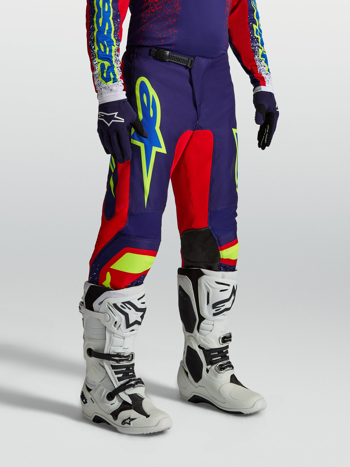 Alpinestars pantaloni Fluid Drag da uomo, abbigliamento motocross blu navy e rosso con grafiche audaci e stivali bianchi.