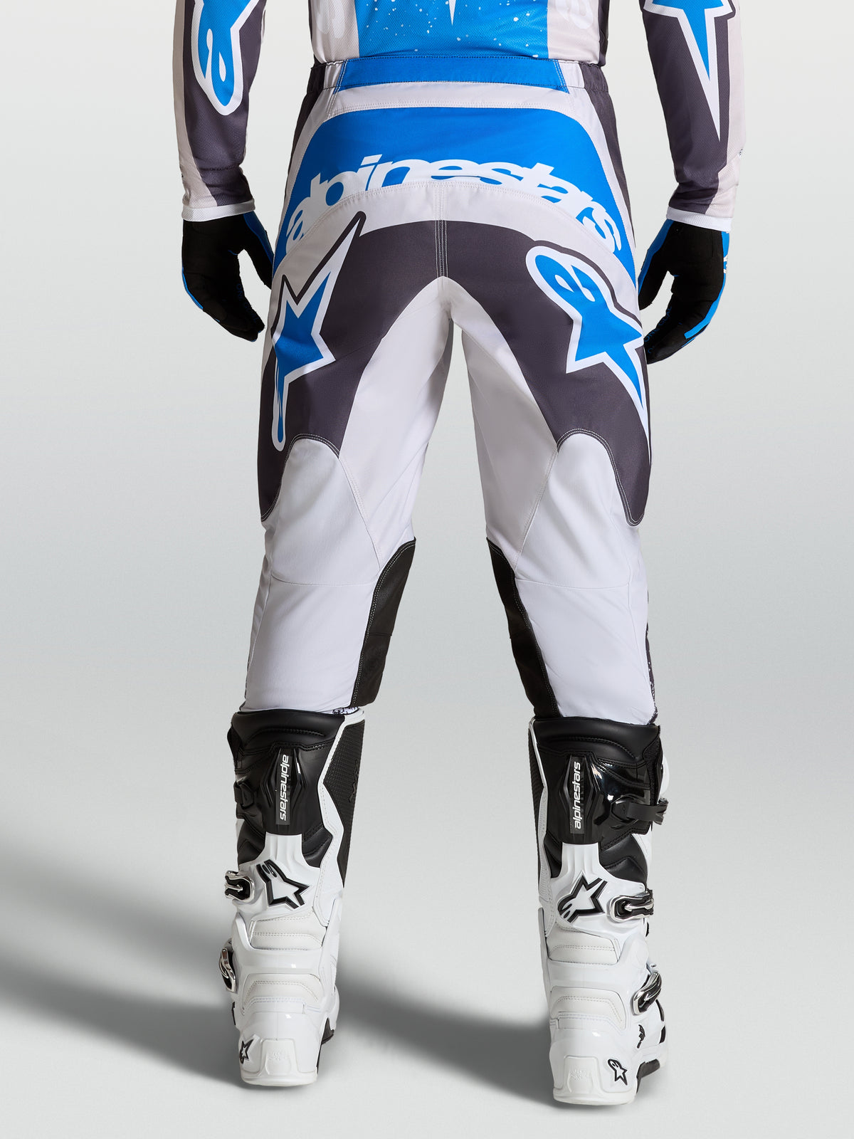 Alpinestars Pantaloni Fluid Drag, pantaloni da motocross per uomo in grigio, blu e bianco, caratterizzati da seduta rinforzata e design ergonomico per la guida off-road, vista posteriore.