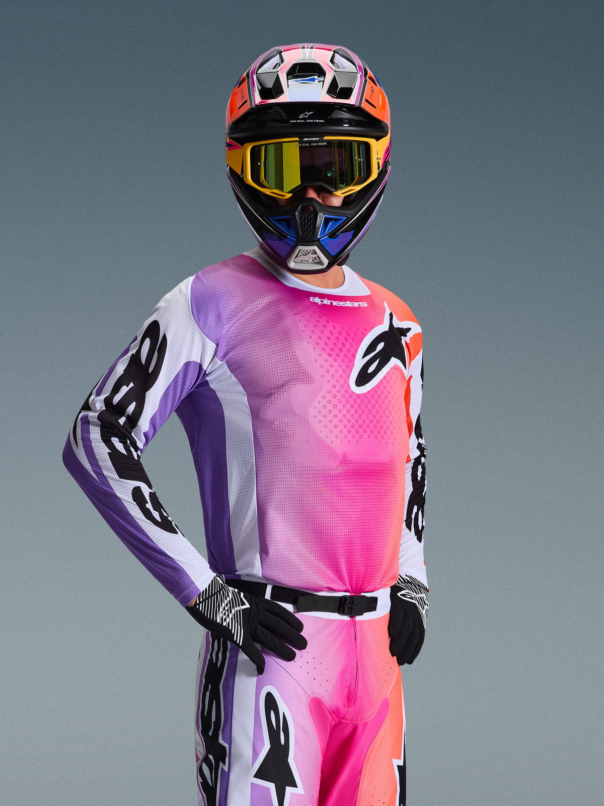 Pilota di motocross con maglia Alpinestars 2026 Racer Air Portl, gradiente multicolore rosa, viola e arancione con accenti bianchi, casco colorato coordinato e maschera gialla, guanti neri, equipaggiamento professionale da gara off-road