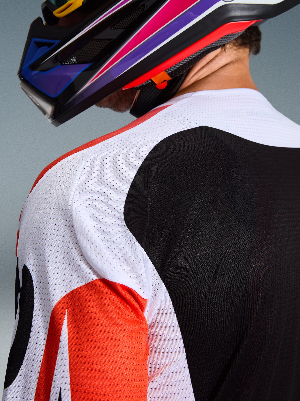 Alpinestars 2026 Racer Air Portl Jersey, maglia da motocross, multicolore con pannelli bianchi, neri e rossi, primo piano della struttura in mesh traforato su spalla e schiena per la ventilazione, indossata con un casco da motocross colorato