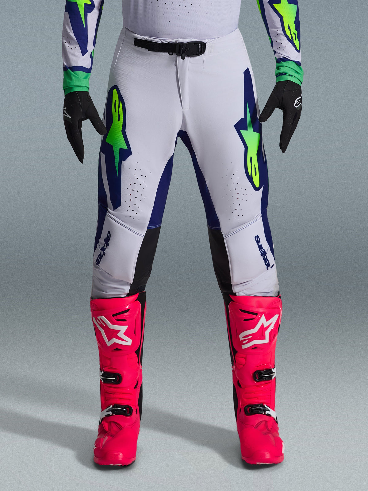 Alpinestars 2026 Supertech Vista Gear Set, pantaloni da motocross bianchi con accenti blu e verde lime, abbinati a stivali rosa vivace e guanti neri, abbigliamento racing professionale con vestibilità atletica e perforazioni laser